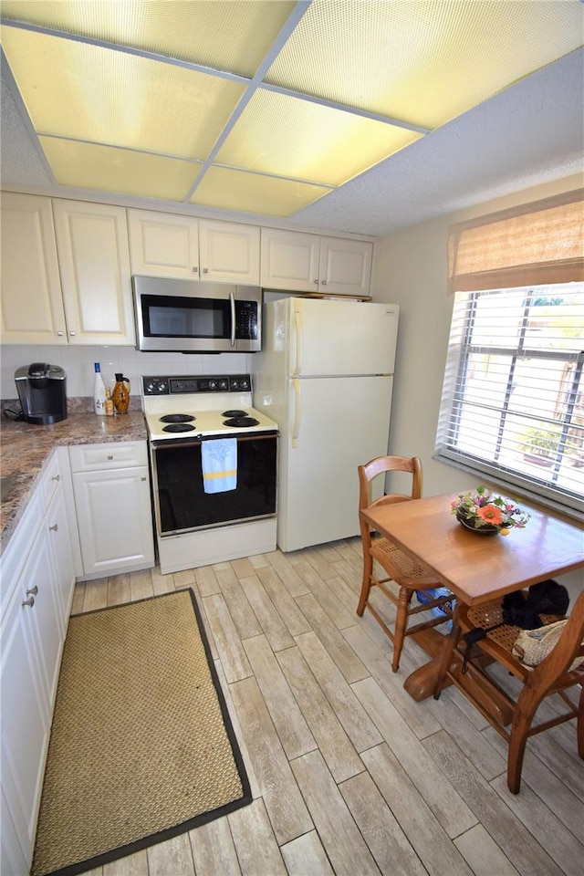 kitchen with white appliances, white cabinetry, and light hardwood / wood-style floors