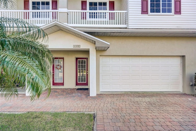 doorway to property featuring a garage, a balcony, and stucco siding