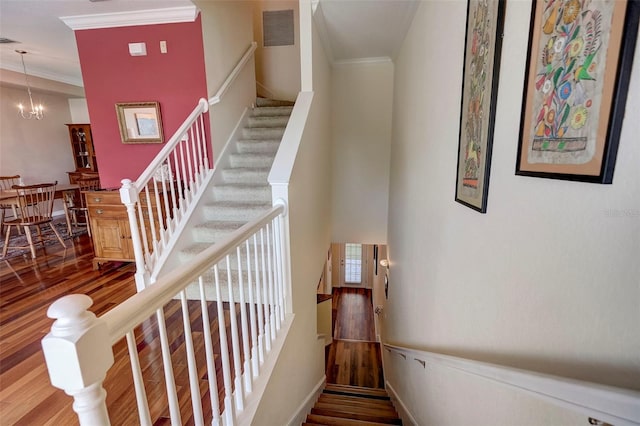 staircase featuring an inviting chandelier, visible vents, crown molding, and wood finished floors