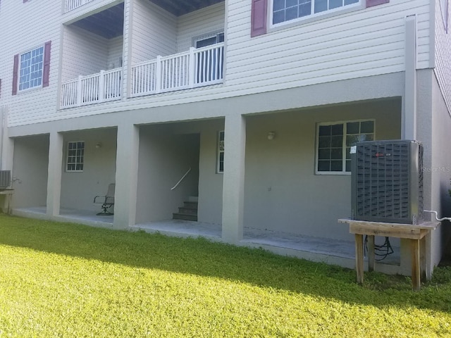 back of house with a balcony, central air condition unit, a patio area, and a yard