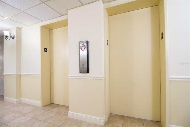 hall with light tile floors, a drop ceiling, and elevator