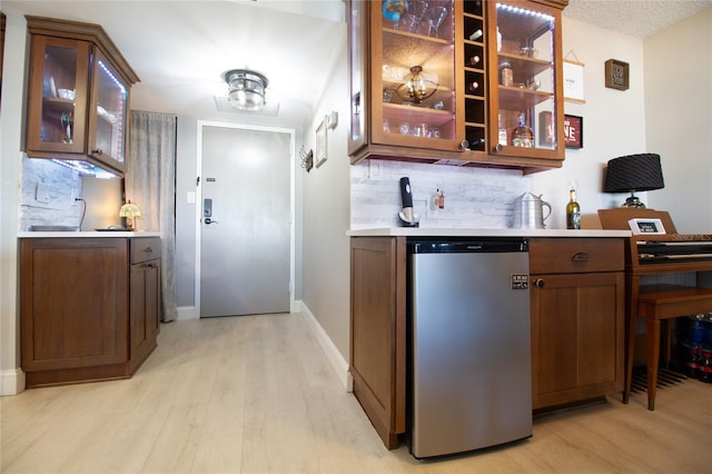 kitchen featuring tasteful backsplash, dark brown cabinetry, stainless steel dishwasher, and light wood-type flooring