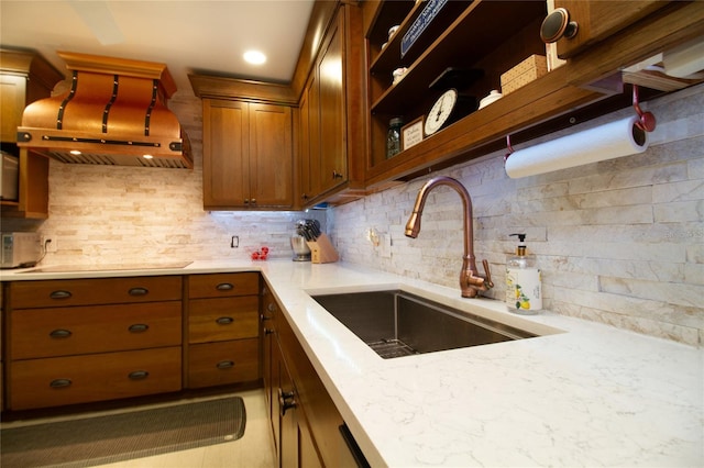 kitchen with light stone counters, backsplash, range hood, and sink