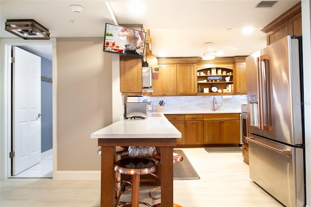 kitchen featuring a kitchen bar, high quality fridge, light hardwood / wood-style floors, and tasteful backsplash