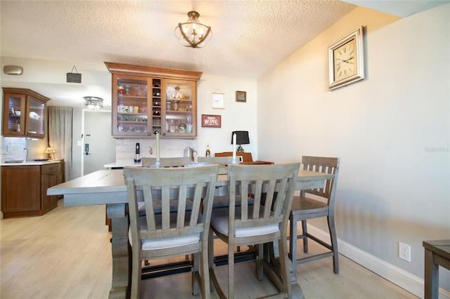 dining area featuring a textured ceiling, a notable chandelier, and light wood-type flooring