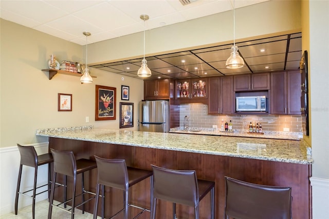 kitchen with pendant lighting, backsplash, appliances with stainless steel finishes, and light stone counters