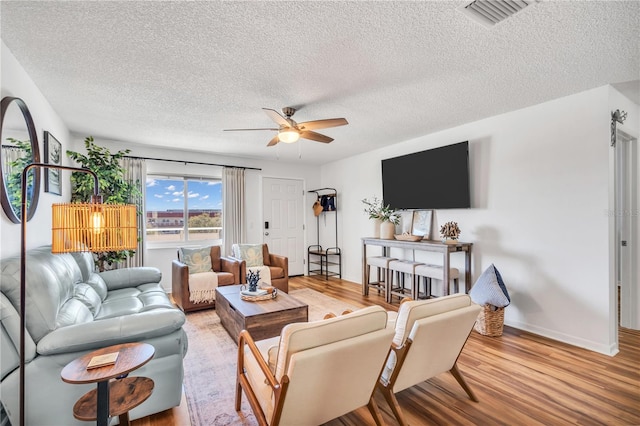 living room with hardwood / wood-style flooring, ceiling fan, and a textured ceiling