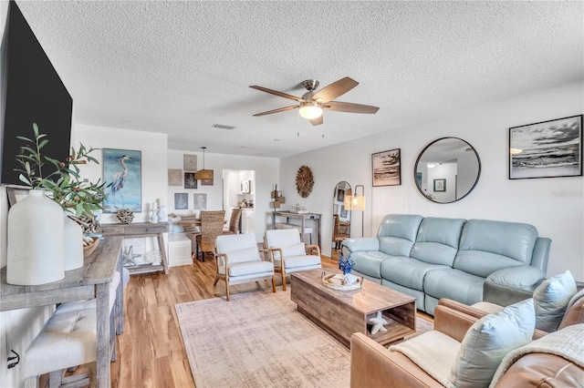 living room featuring ceiling fan, light hardwood / wood-style floors, and a textured ceiling