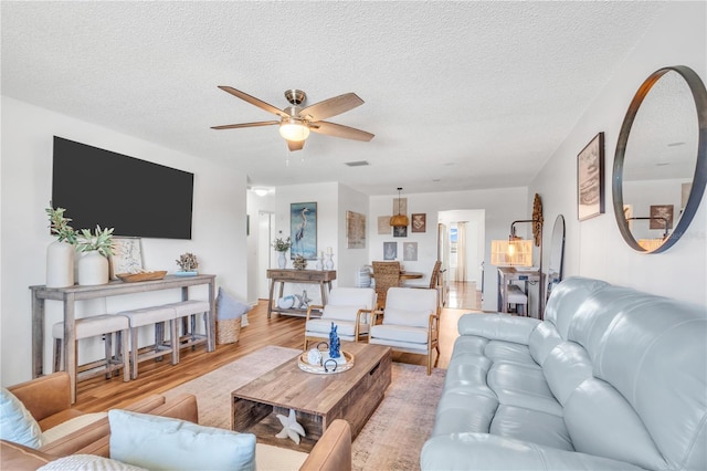 living room with ceiling fan, light hardwood / wood-style floors, and a textured ceiling