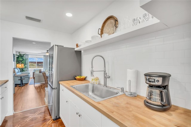 kitchen with white cabinets, stainless steel fridge, butcher block counters, and sink