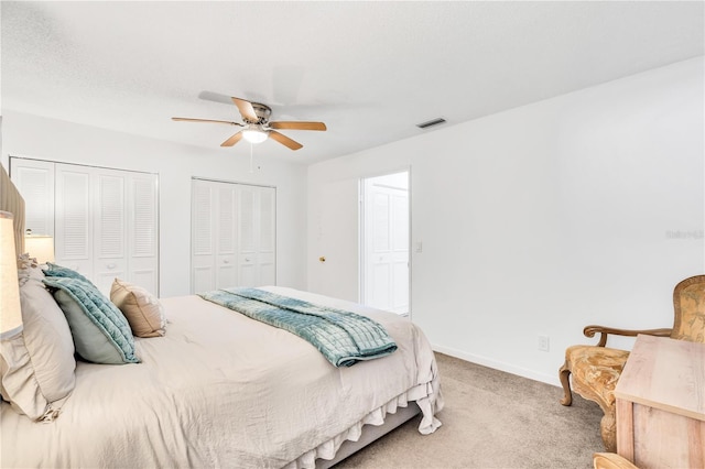 carpeted bedroom with ceiling fan and two closets