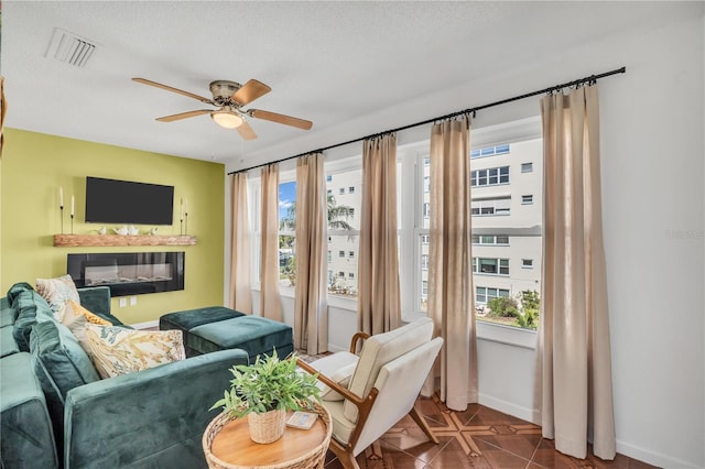 living area featuring tile patterned flooring, ceiling fan, a healthy amount of sunlight, and a textured ceiling