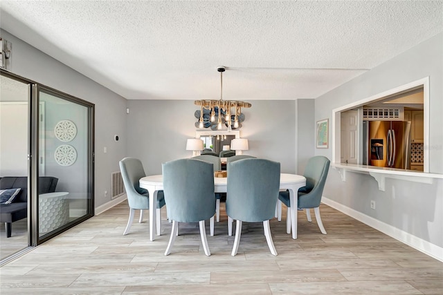 dining room with a textured ceiling, a chandelier, and light wood-type flooring