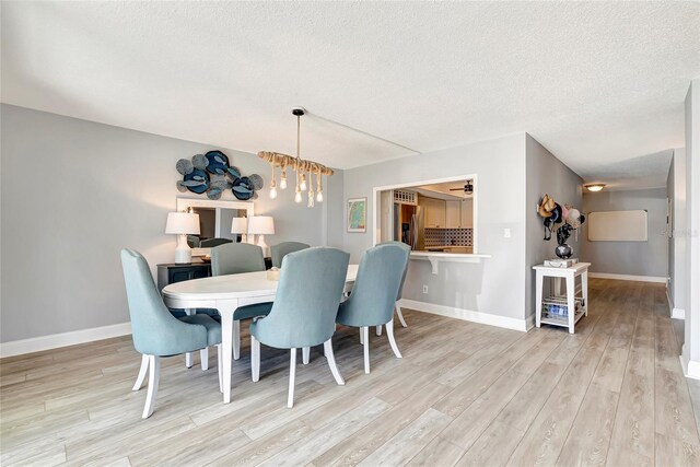 dining space with a textured ceiling, a notable chandelier, and light wood-type flooring