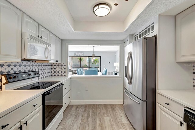 kitchen with backsplash, a tray ceiling, white appliances, light hardwood / wood-style flooring, and white cabinets