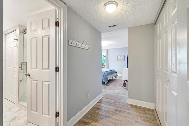 hall with a textured ceiling and light hardwood / wood-style flooring