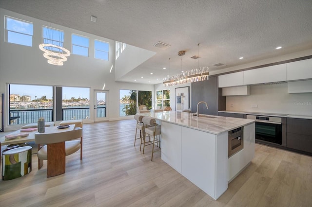 kitchen with hanging light fixtures, white cabinets, appliances with stainless steel finishes, light hardwood / wood-style flooring, and a center island with sink