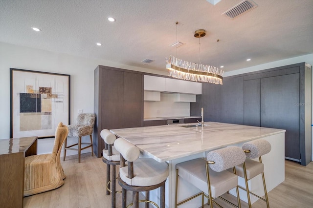 kitchen with a kitchen bar, an island with sink, white cabinets, and light hardwood / wood-style flooring