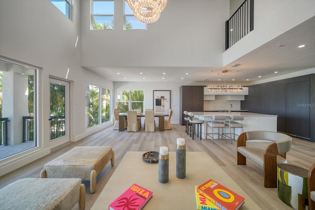 living room featuring light hardwood / wood-style flooring, sink, a chandelier, and a towering ceiling