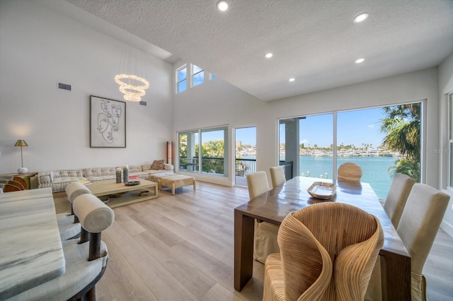 interior space featuring light hardwood / wood-style flooring, a water view, a textured ceiling, a chandelier, and a towering ceiling