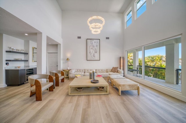 living room featuring a towering ceiling, light hardwood / wood-style flooring, an inviting chandelier, and wine cooler