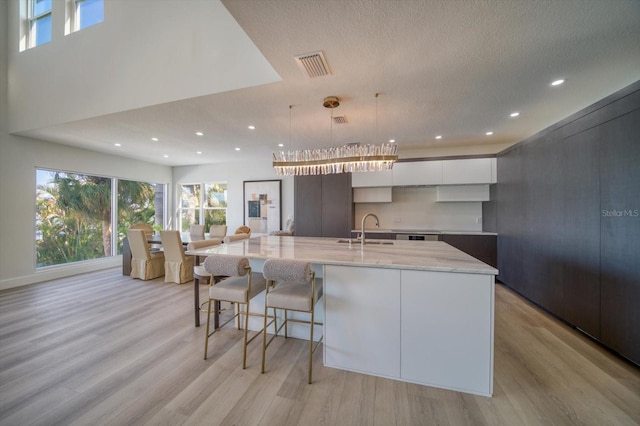 kitchen with an island with sink, pendant lighting, plenty of natural light, light hardwood / wood-style flooring, and white cabinetry