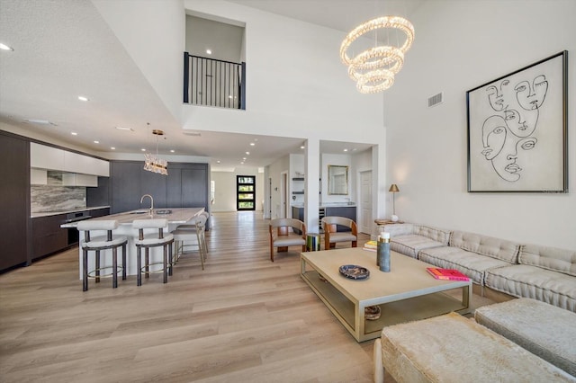 living room with a chandelier, a high ceiling, light wood-type flooring, and sink