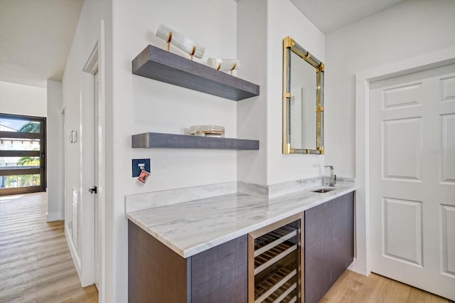 bar featuring wine cooler, light stone countertops, sink, and light wood-type flooring