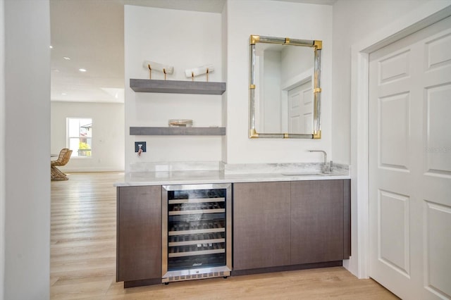 bar featuring beverage cooler, light hardwood / wood-style flooring, dark brown cabinetry, and sink