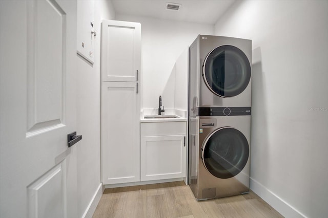 laundry area featuring stacked washer / drying machine, light hardwood / wood-style flooring, cabinets, and sink