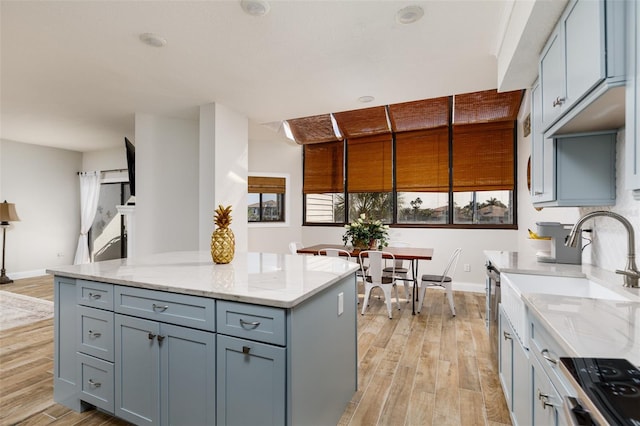 kitchen with gray cabinetry, stove, light hardwood / wood-style floors, and light stone counters