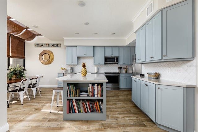 kitchen featuring stainless steel appliances, a center island, a kitchen bar, tasteful backsplash, and ornamental molding