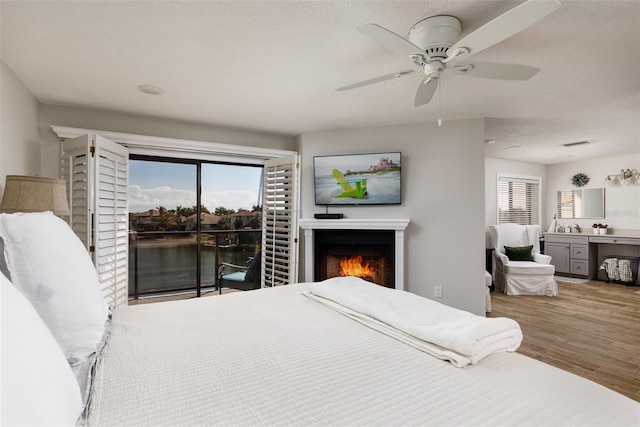 bedroom featuring a water view, hardwood / wood-style floors, ceiling fan, and access to outside