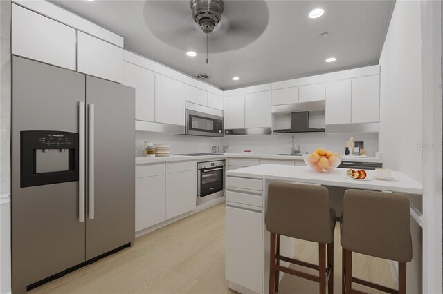 kitchen with a kitchen breakfast bar, stainless steel appliances, ceiling fan, light hardwood / wood-style flooring, and white cabinetry