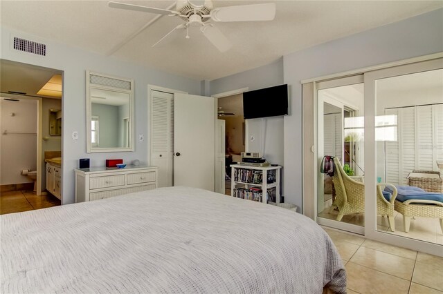 bedroom with connected bathroom, light tile patterned floors, two closets, and ceiling fan