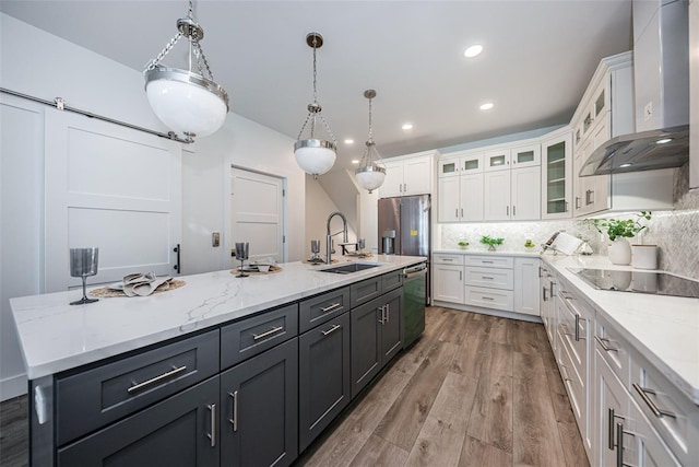 kitchen featuring white cabinetry, wall chimney range hood, an island with sink, and decorative light fixtures