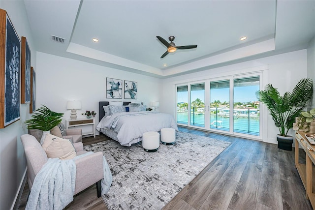 bedroom with access to outside, ceiling fan, a tray ceiling, and dark wood-type flooring