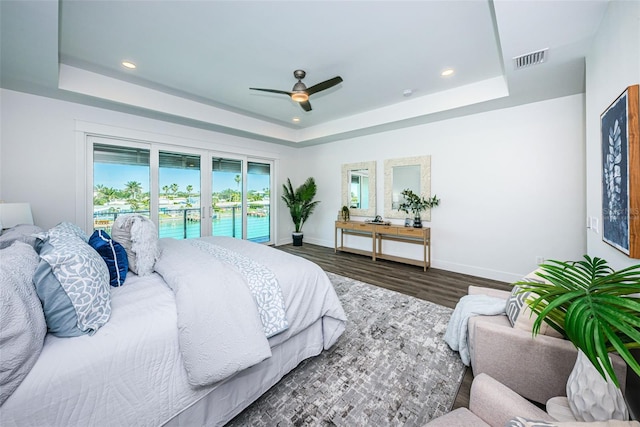 bedroom featuring dark hardwood / wood-style flooring, ceiling fan, access to outside, and a tray ceiling