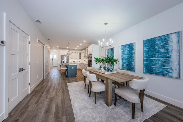 dining space featuring sink, a barn door, dark hardwood / wood-style floors, and an inviting chandelier