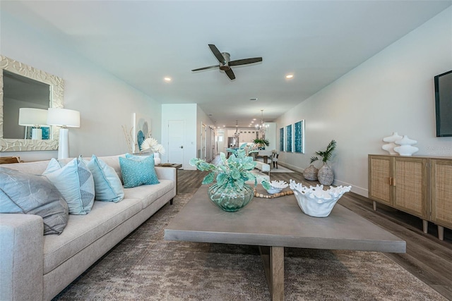 living room featuring ceiling fan with notable chandelier and dark wood-type flooring