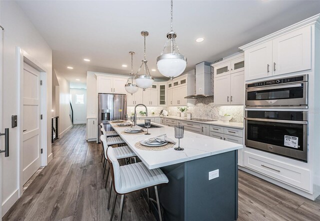 kitchen with wall chimney exhaust hood, a kitchen breakfast bar, backsplash, appliances with stainless steel finishes, and hardwood / wood-style flooring