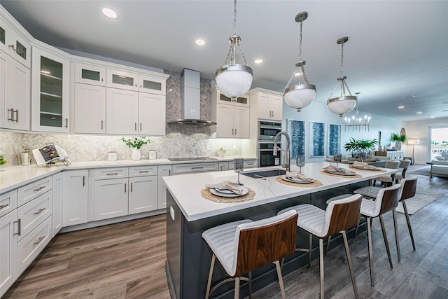 kitchen featuring decorative light fixtures, backsplash, a center island with sink, dark wood-type flooring, and wall chimney range hood