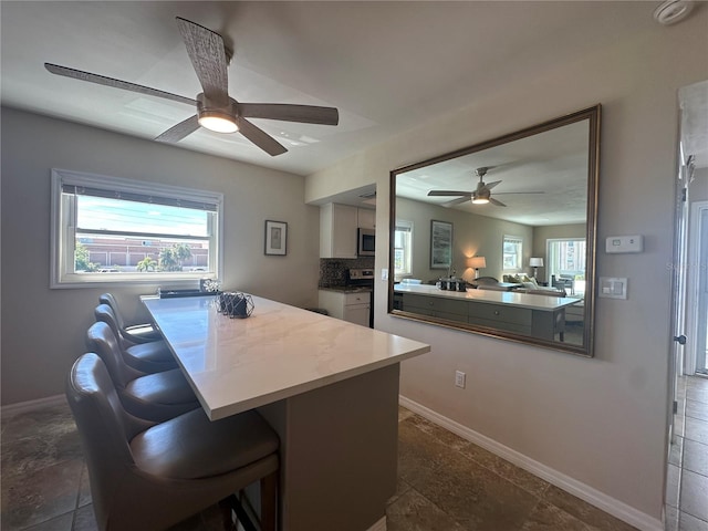 interior space featuring ceiling fan, decorative backsplash, white cabinets, and a kitchen bar