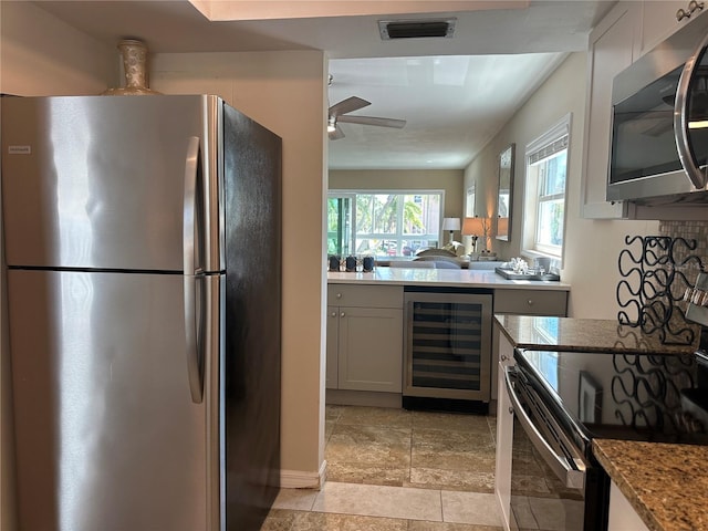 kitchen with white cabinets, beverage cooler, ceiling fan, light stone counters, and stainless steel appliances