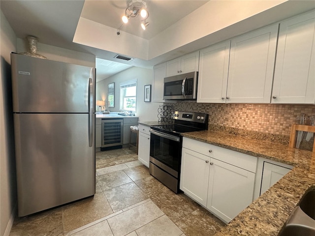 kitchen with white cabinetry, stainless steel appliances, wine cooler, a tray ceiling, and dark stone counters