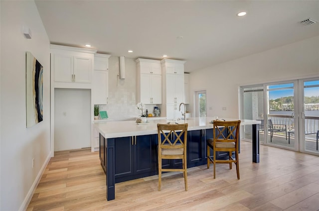 kitchen featuring white cabinetry, a center island with sink, tasteful backsplash, light hardwood / wood-style floors, and a kitchen bar