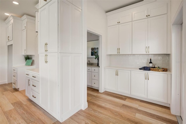 kitchen featuring backsplash, sink, light hardwood / wood-style flooring, and white cabinets