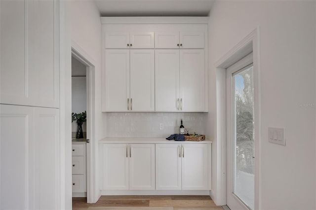 bar featuring light hardwood / wood-style floors, decorative backsplash, and white cabinets