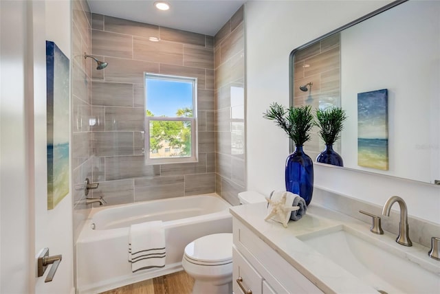 full bathroom featuring vanity, hardwood / wood-style floors, tiled shower / bath combo, and toilet