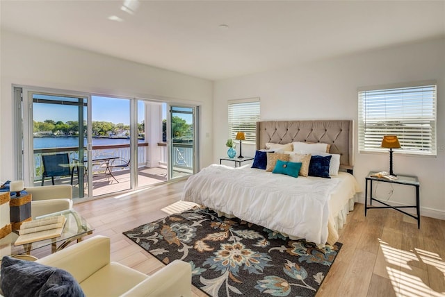 bedroom with a water view, multiple windows, light hardwood / wood-style flooring, and access to outside